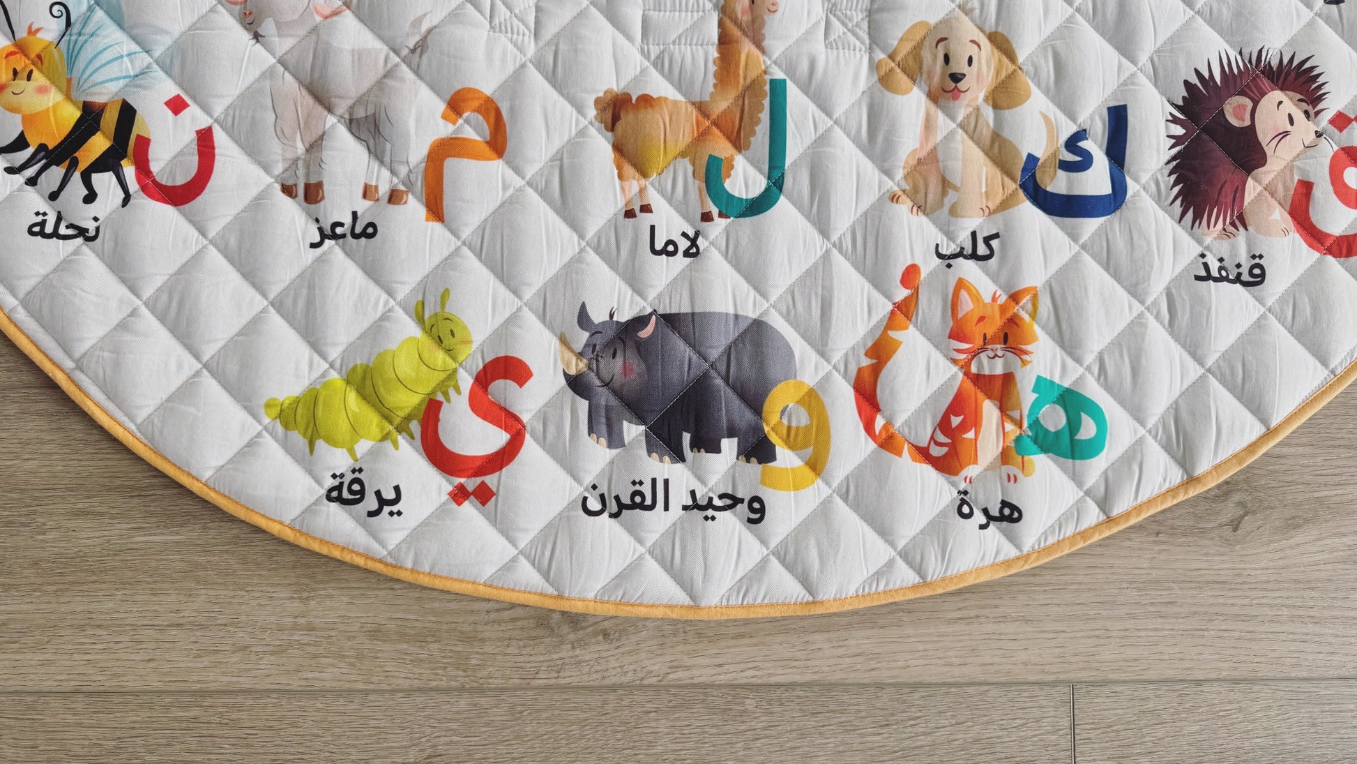 Children's educational rug with animal illustrations and Arabic text on a wooden floor.